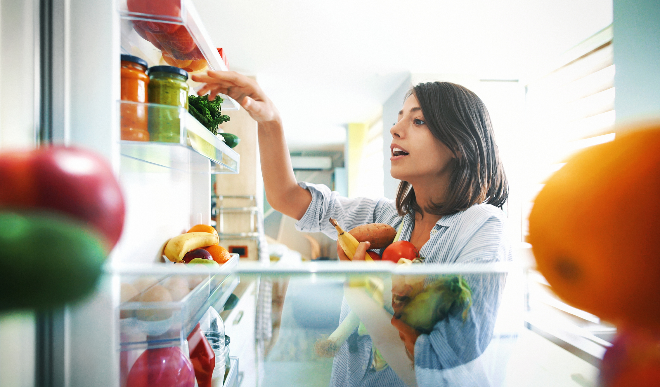 Closeup of a cheerful young couple picking some fruit and veggies from the fridge to make some healthy breakfast on Sunday morning. Shot from inside the working fridge.