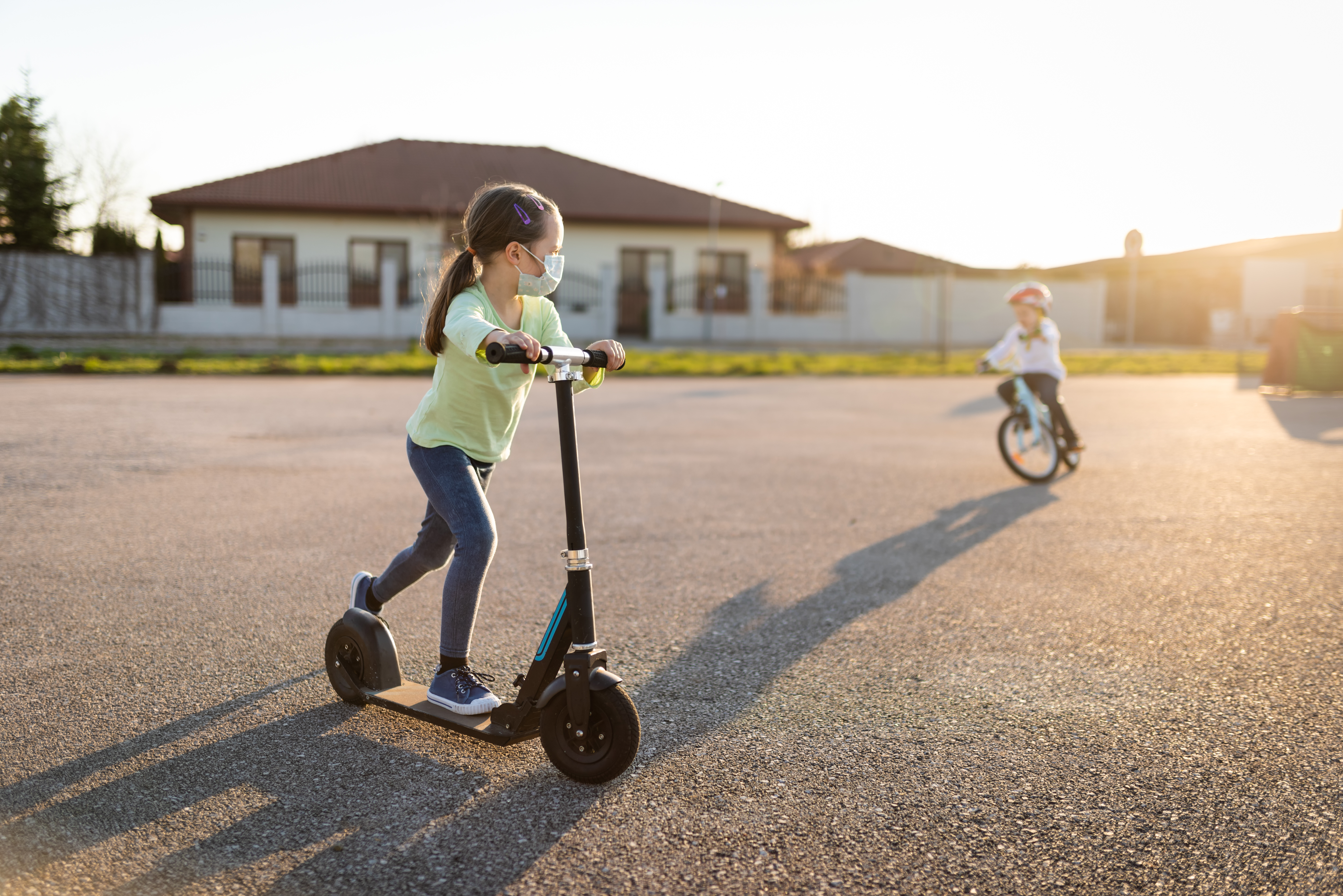 Child with protective face mask riding on scooter during corona virus pandemic