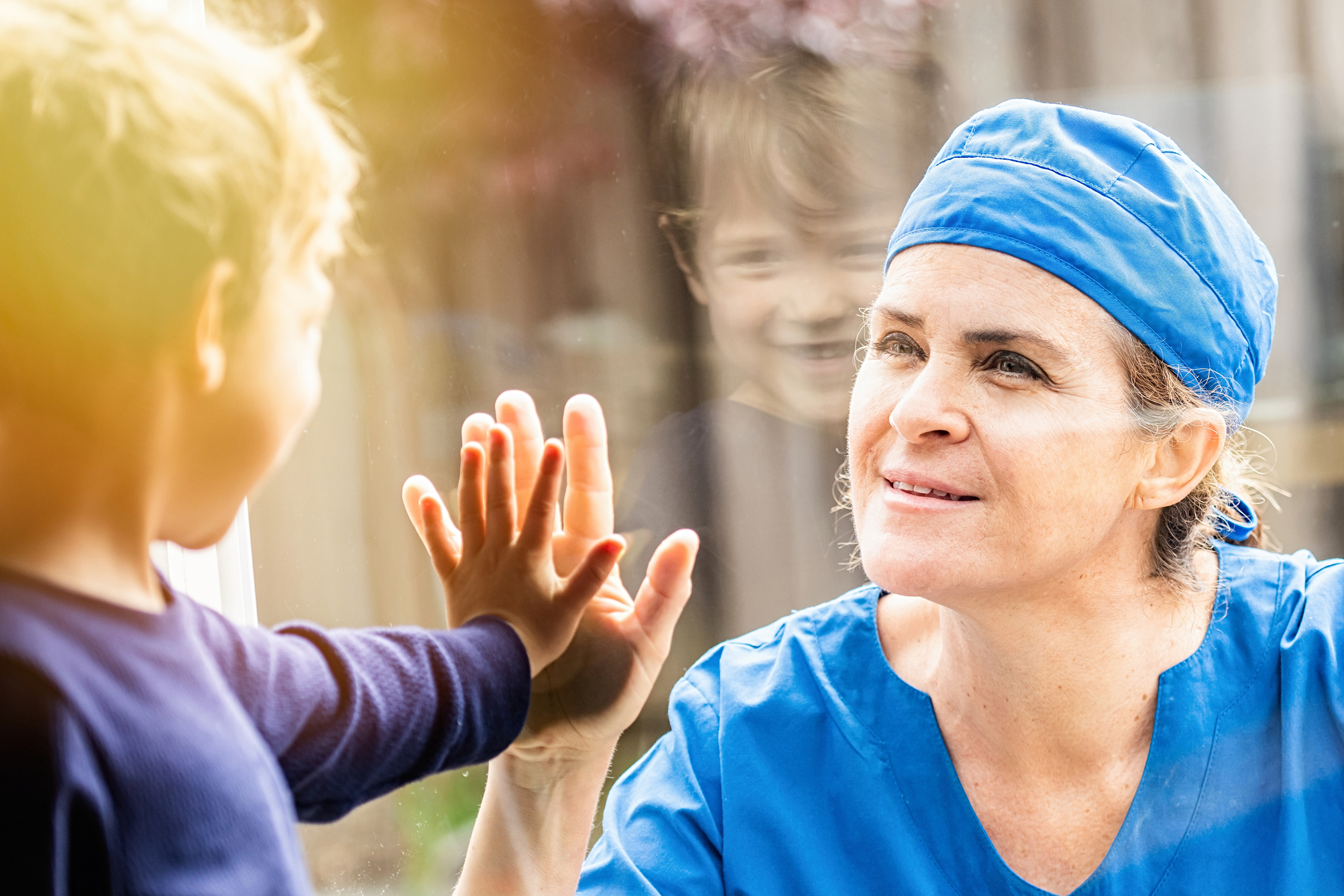 Caucasian Mature Healthcare worker posing seeing her son with a window glass separating them to avoid possible contagion