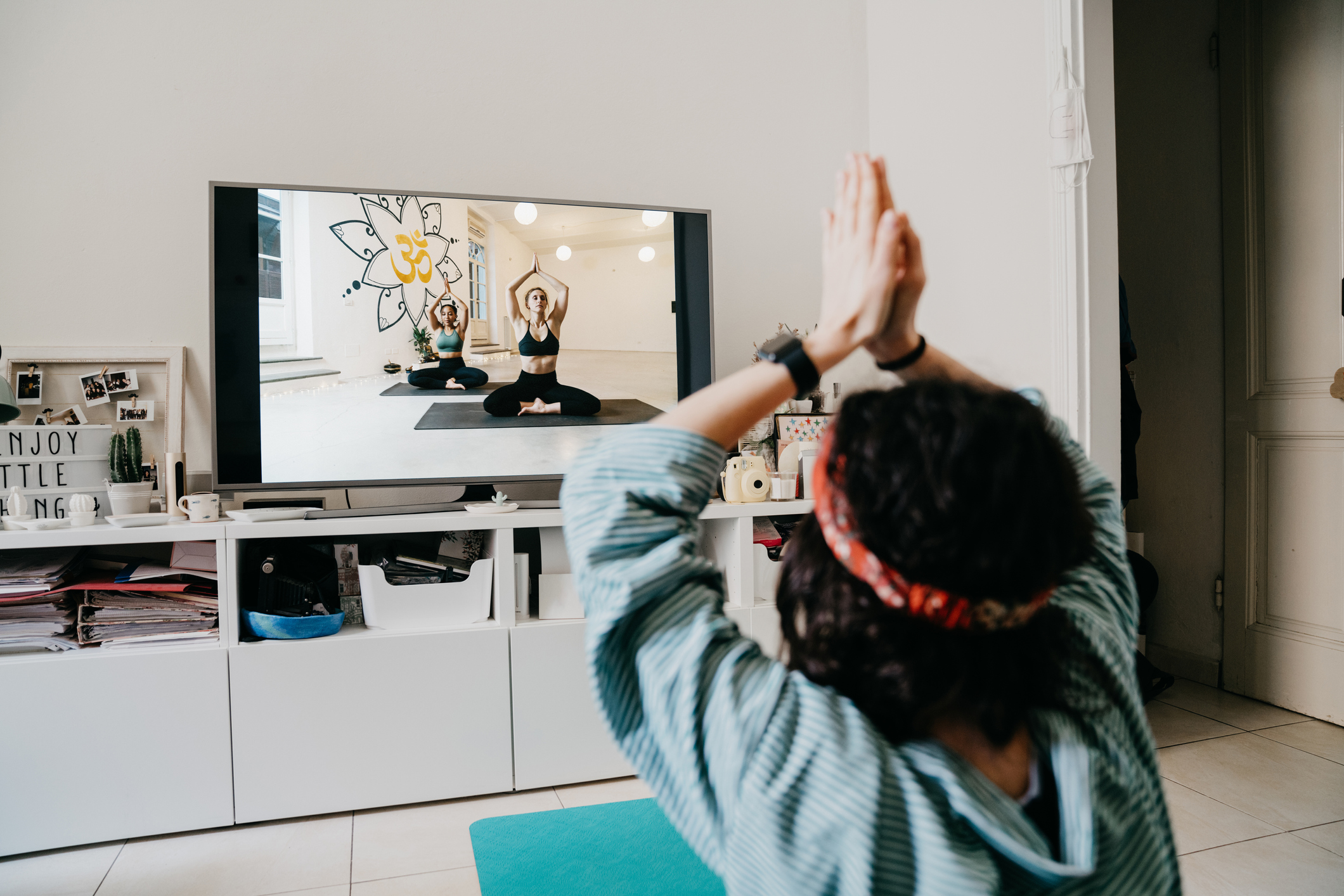 Woman practicing yoga at home with a video lesson on the TV. She's at home during the Coronavirus Covid-19 quarantine.