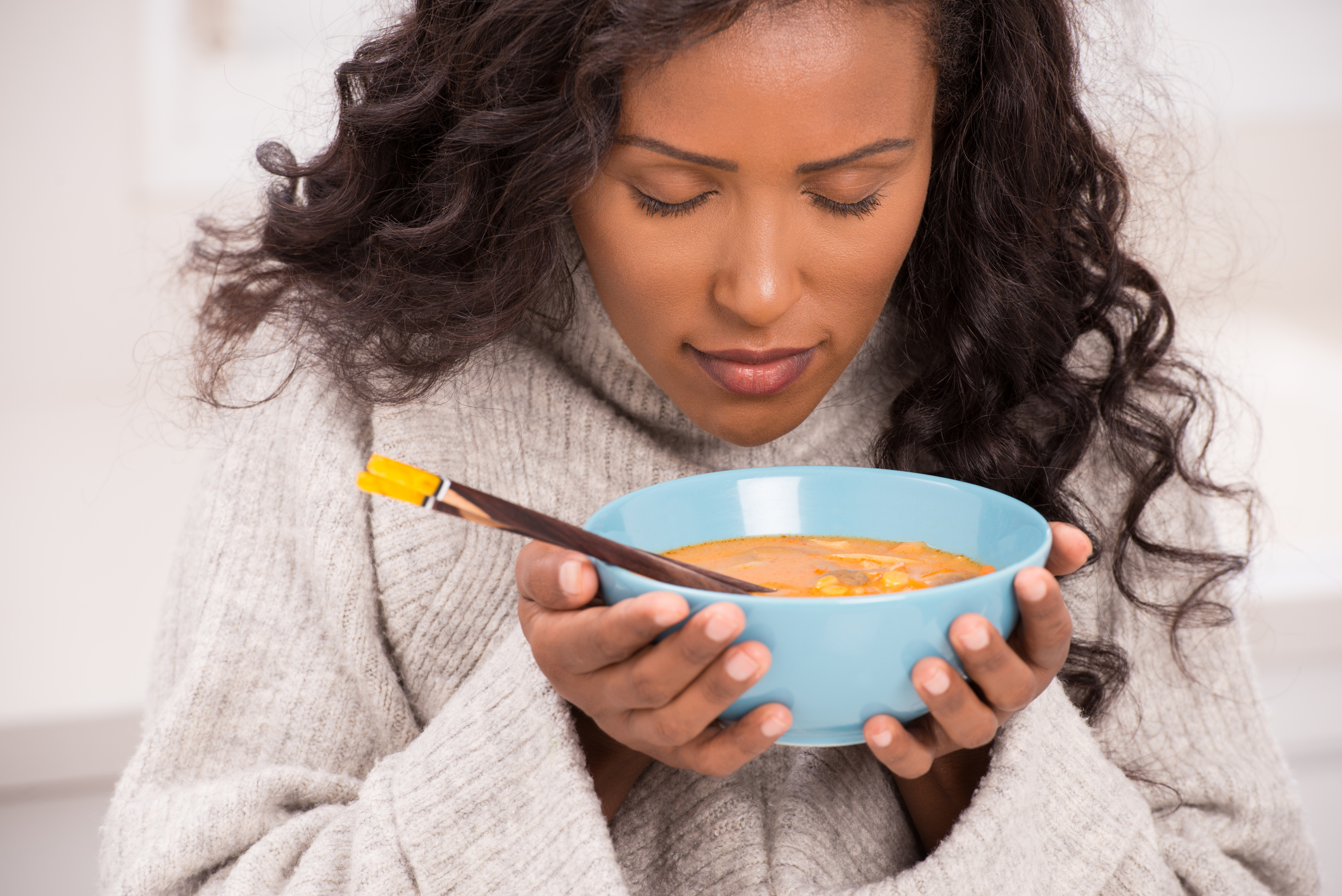 Beautiful young woman eating tom Yum soup, closing her eyes enjoying aroma of delicious soup.