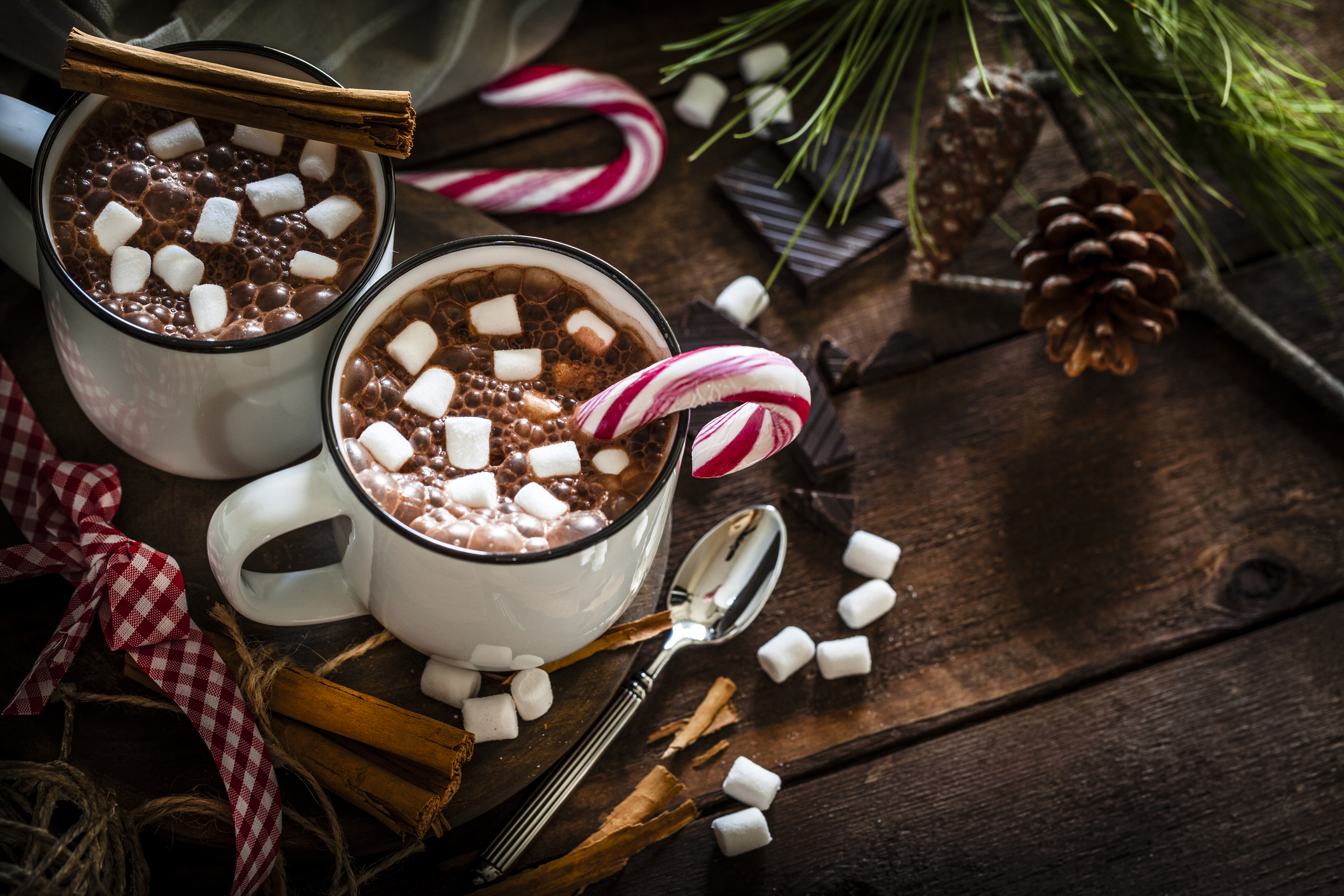 High angle view of two homemade hot chocolate mugs with marshmallows shot on rustic wooden Christmas table. A candy cane is inside one mug and another is placed directly on the table. Christmas decoration complete the composition. Low key DSRL studio photo taken with Canon EOS 5D Mk II and Canon EF 100mm f/2.8L Macro IS USM