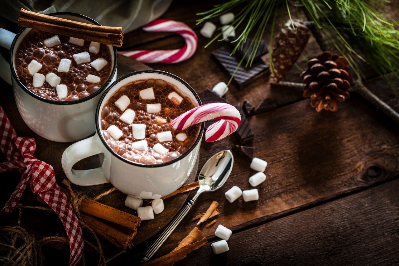 High angle view of two homemade hot chocolate mugs with marshmallows shot on rustic wooden Christmas table. A candy cane is inside one mug and another is placed directly on the table. Christmas decoration complete the composition. Low key DSRL studio photo taken with Canon EOS 5D Mk II and Canon EF 100mm f/2.8L Macro IS USM