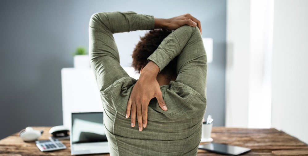 Person at table with laptop, stretching arms over head.