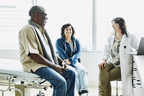 Smiling female doctor consulting with senior male patient and adult daughter in exam room