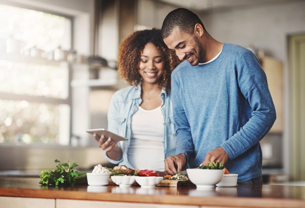 Shot of a happy young couple using a digital tablet while preparing a healthy meal together at home