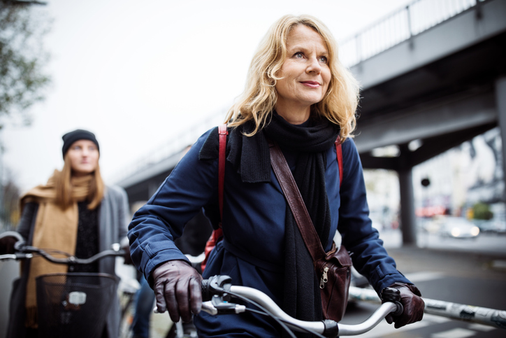 Smiling mature woman riding bicycle. Friends traveling together in city. They are in warm clothing.