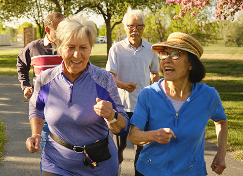 A group of senior aged men and women power walking in a park.