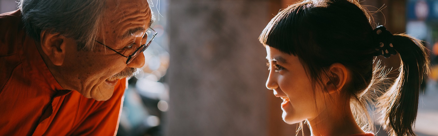 Profile view of cute young mixed race girl smiling at her Japanese grandfather with sunlight on street