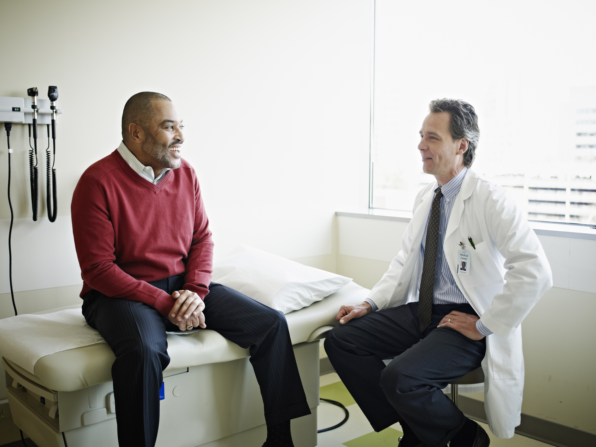 Mature male patient sitting on exam table in discussion with doctor in exam room