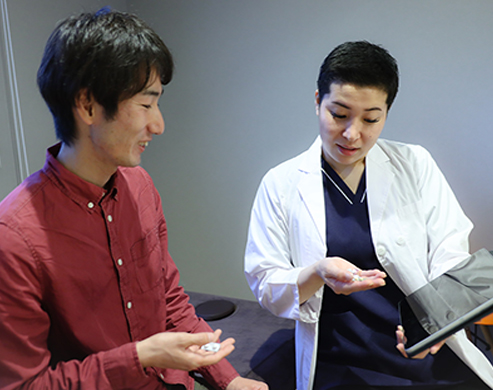 Young non-binary pharmacist explaining to a young asian patient. Pharmacist uses a tablet to explain details of medicine to a patient.