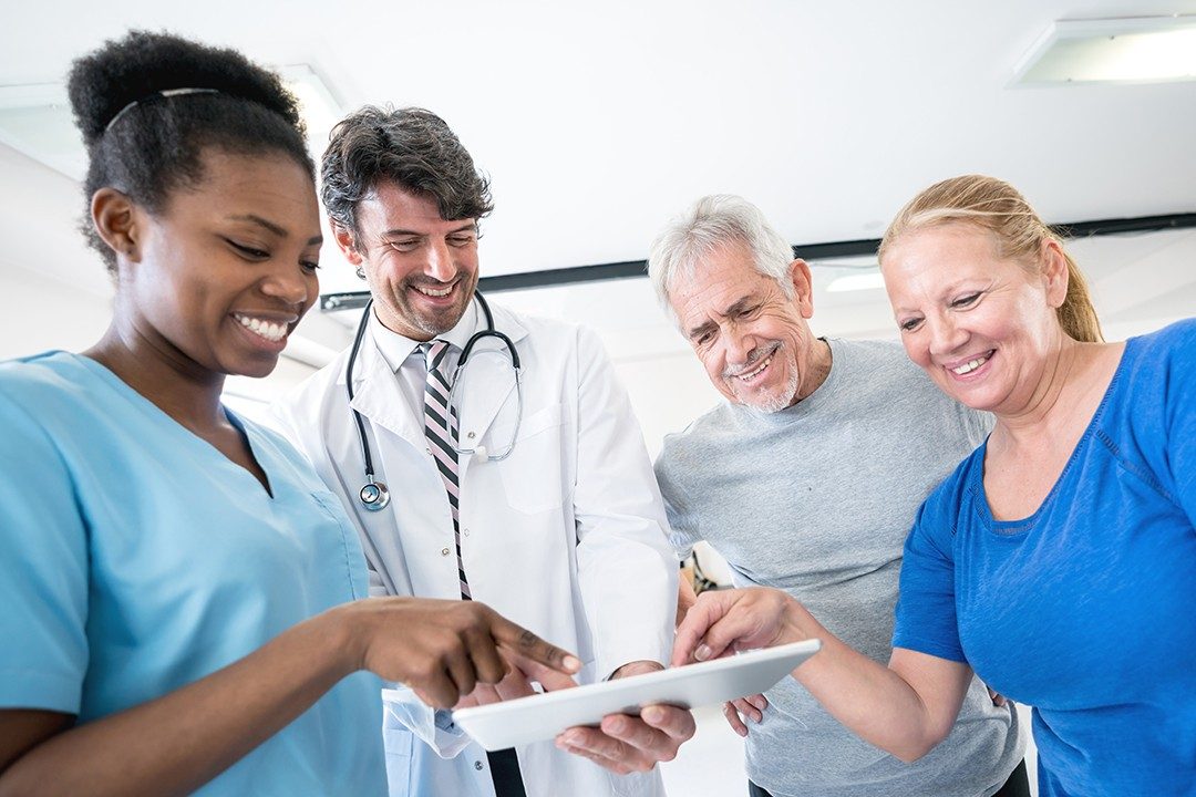 Doctor and nurse showing their senior patients something on a tablet while pointing all looking very happy and smiling