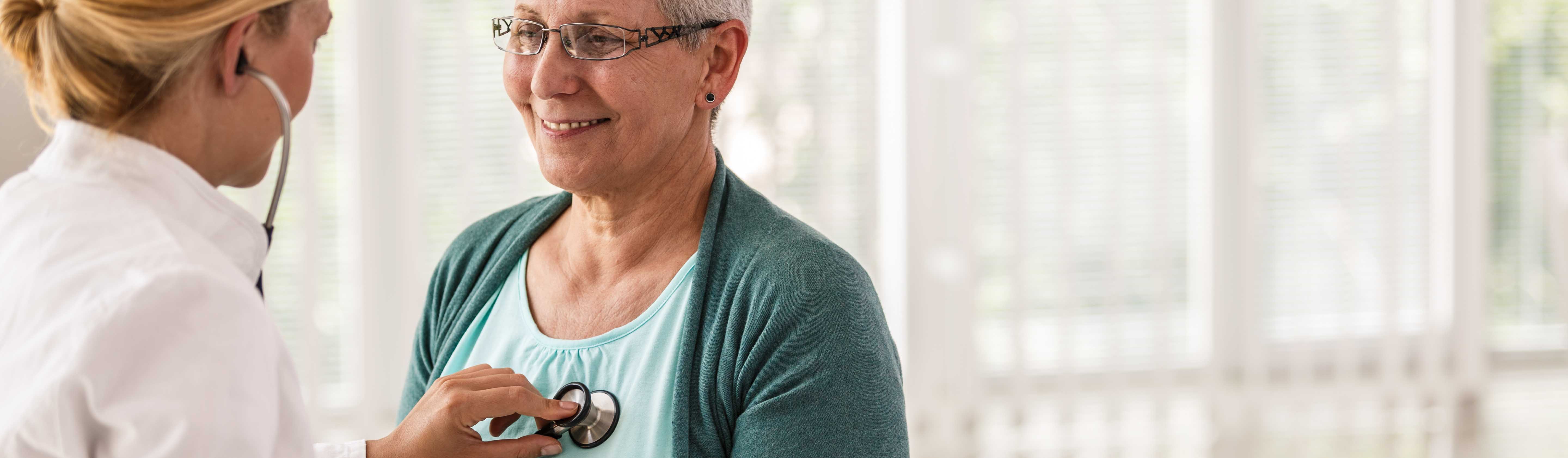 Female doctor listening senior woman's heartbeat during routine medical examination.