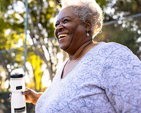 A senior smiling woman drinking water in a sunny park