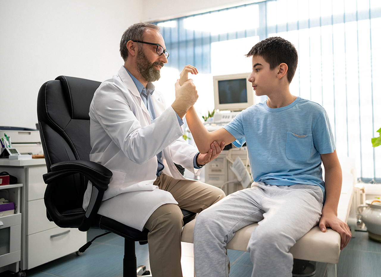 A mature doctor examines his young patient. Doctor checks the condition of the boy's arm.