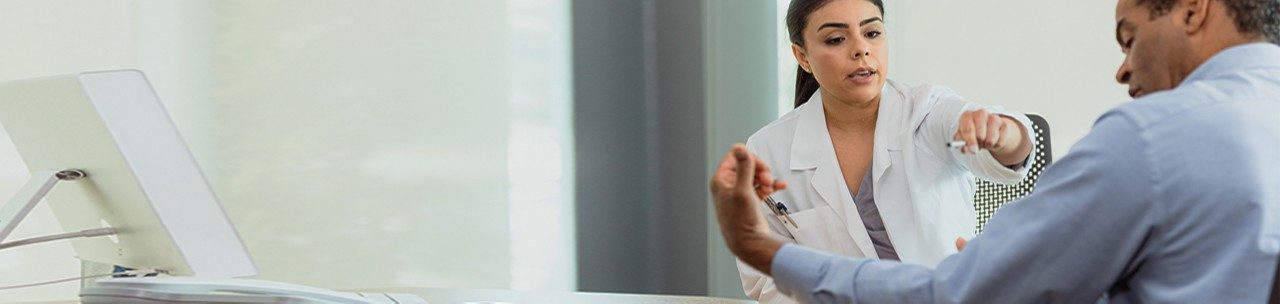 A mid adult female doctor asks a mature male patient questions about the pain in his arm. The man gestures to an area on his arm.