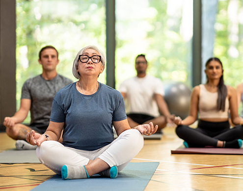A diverse group of adults meditate on their yoga mats in a gymnasium. 