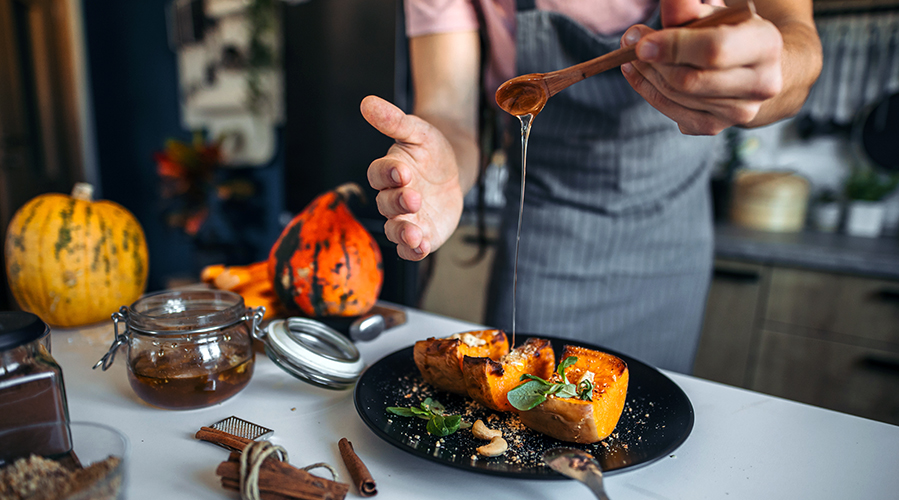 A young man in the rustic kitchen preparing and serving healthy dessert. Pumpkin with cinnamon and honey.